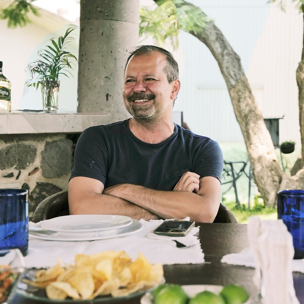 juan eduardo tequila el viejito Man sitting at an outdoor table with a plate of food and blue glasses.