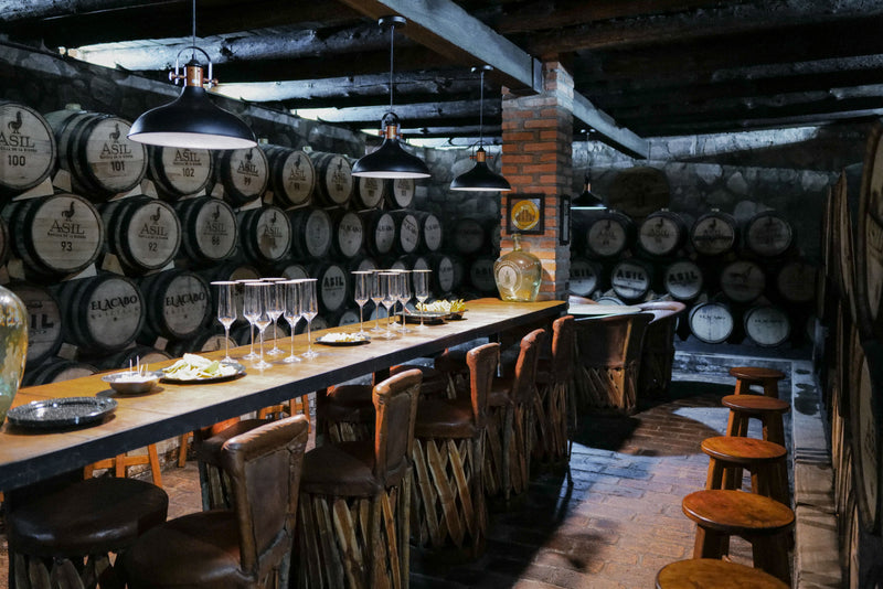 Bar with wooden barrels, glasses, and stools in a rustic setting