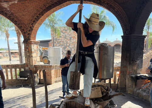 Person in cowboy hat using a long tool inside an archway with a rustic setting