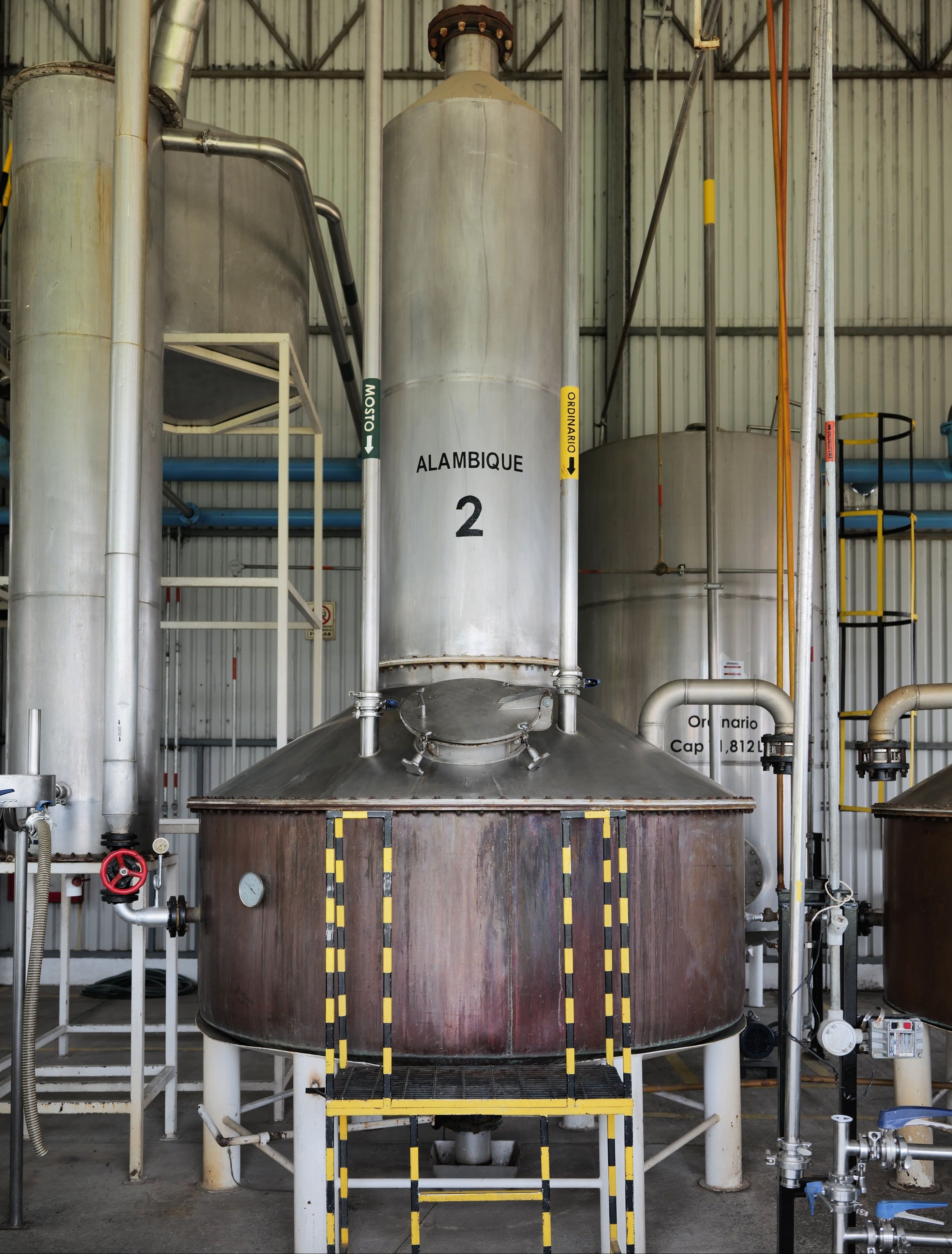 Large metal still with 'Alambique 2' marking in a industrial setting