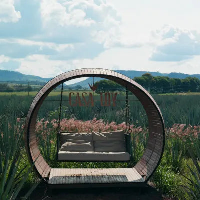 Circular wooden swing in an agave field with 'Casa Loy' branding, surrounded by greenery and mountains.