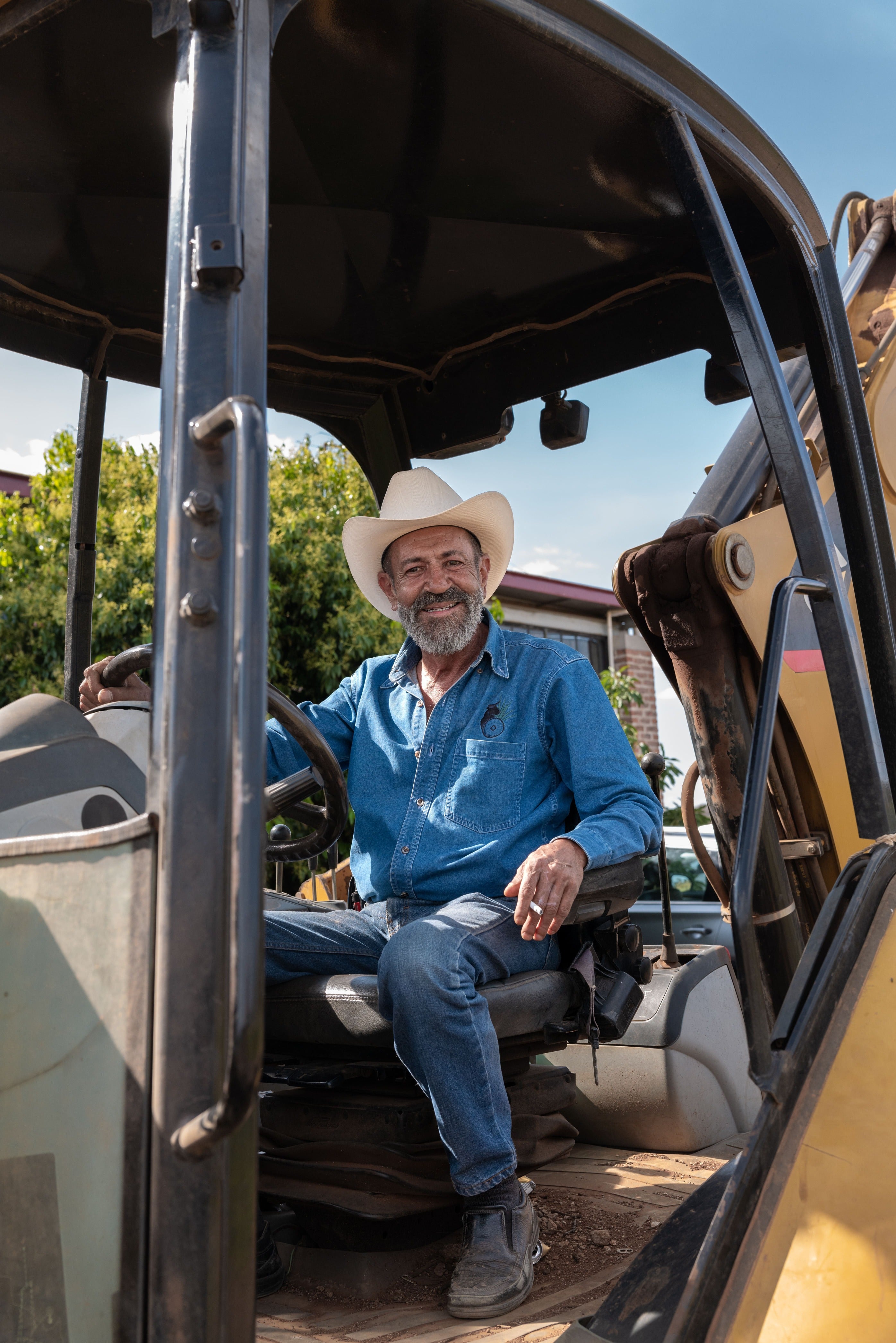 felipe camarena tequila tour Man sitting inside a large piece of construction equipment with a clear sky and trees in the background.