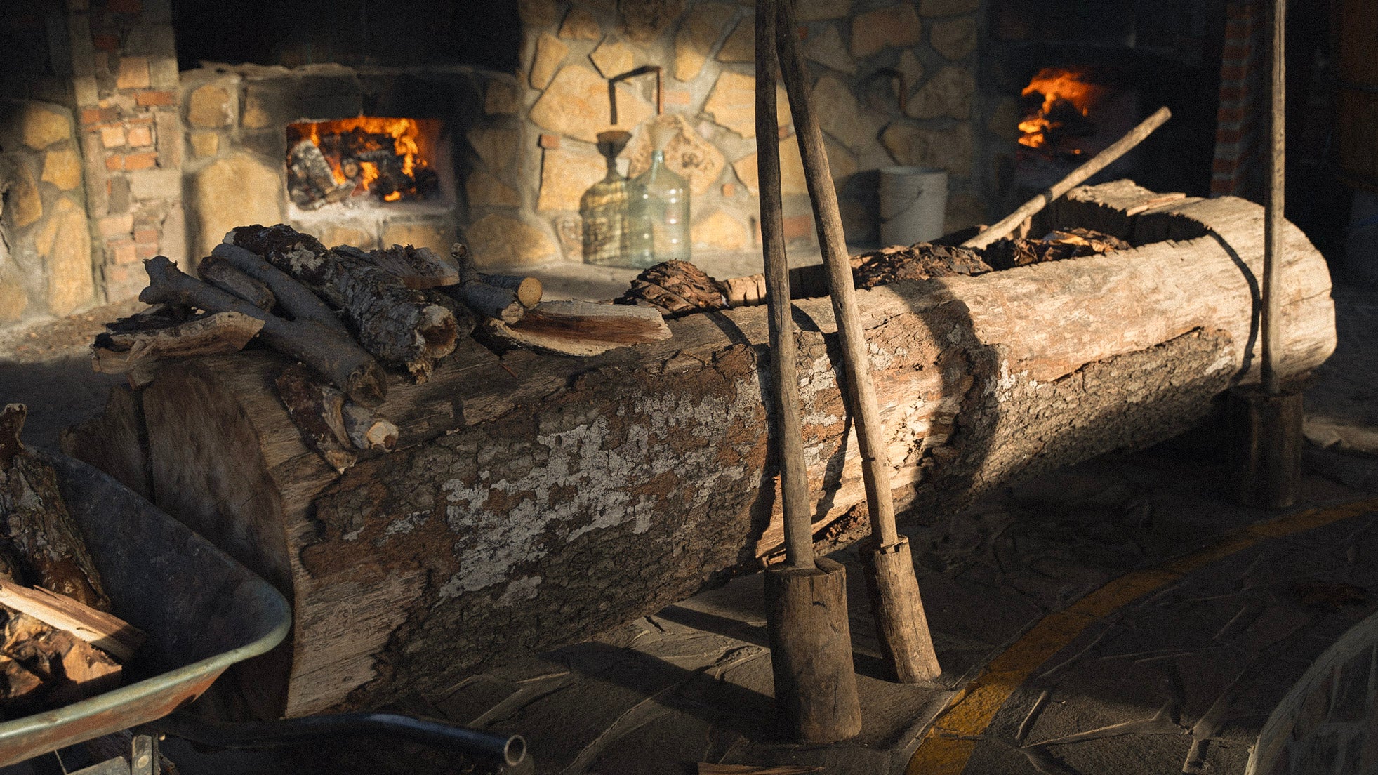 Wooden log with tools on a stone hearth with a fire burning in the background
